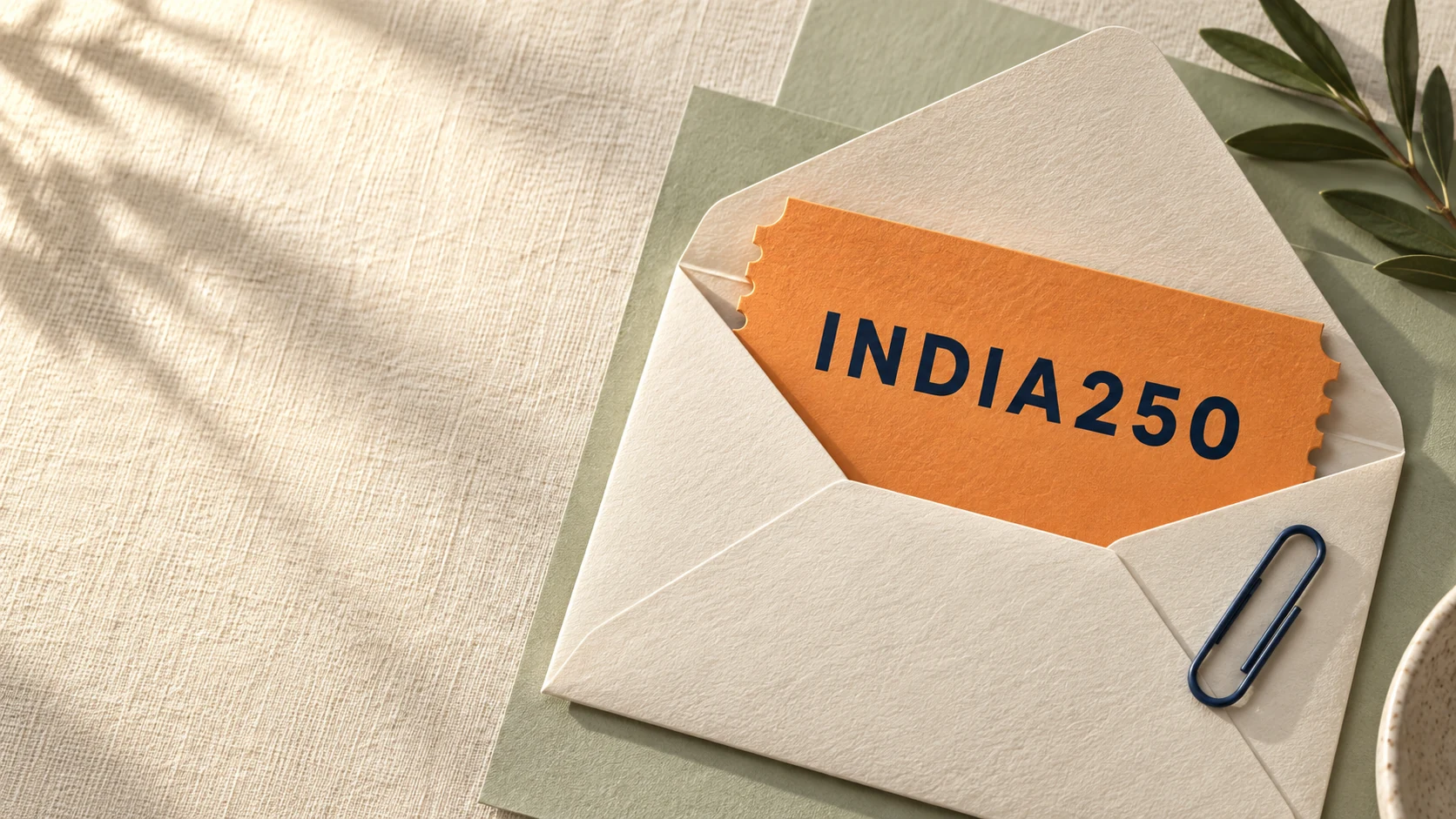 An amber INDIA250 voucher tucked into an ivory envelope on layered sage paper